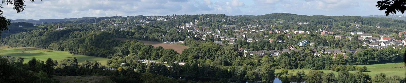 Weiter Blick über das Ruhrtal auf den bewaldeten Hang von Bommern, dazwischen Wohnhäuser, Wiesen und Äcker, unten die Ruhr.