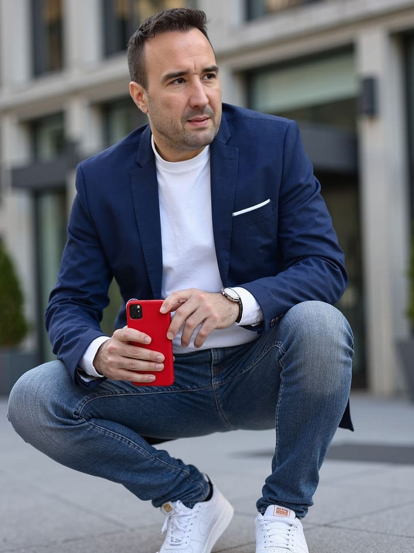 Christian Gottschling hockt mit einem roten Smartphone in der Hand vor einem modernen Bürogebäude
