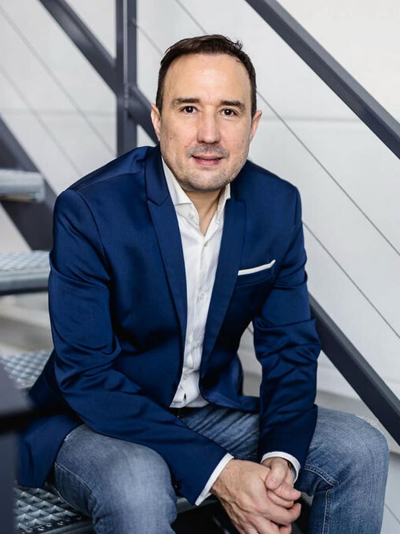 Christian Gottschling sitzt im blauen Sakko über Jeans auf einer Metalltreppe